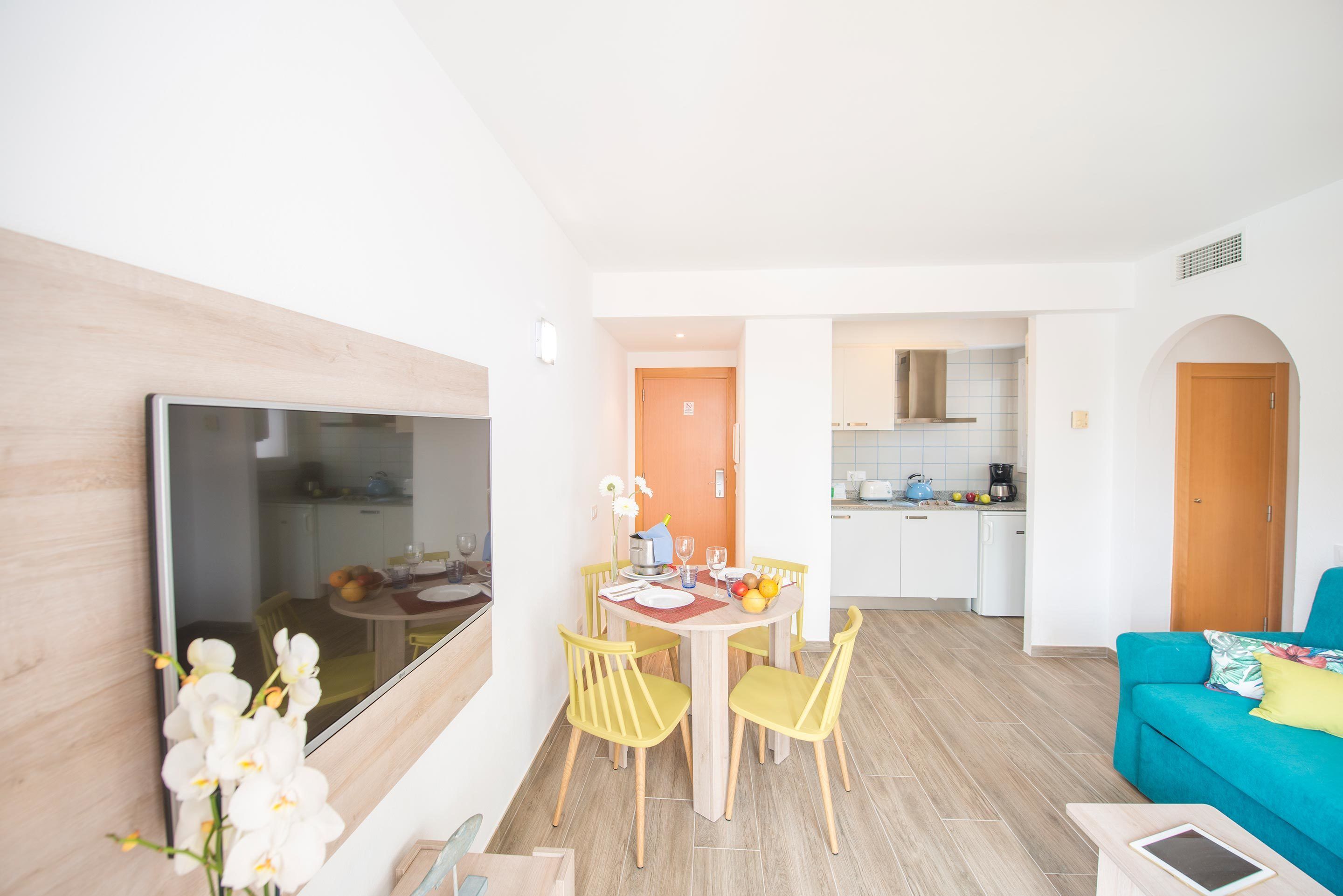 Uma sala de estar moderna com área de jantar, cozinha ao fundo e uma televisão grande na parede.