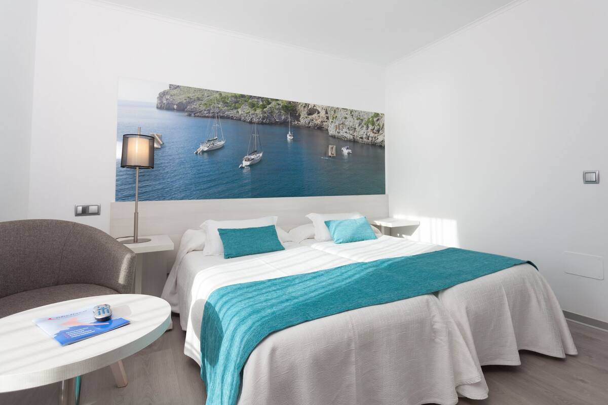 Habitación de hotel con cama, una silla, una mesita y una lámpara de pared.