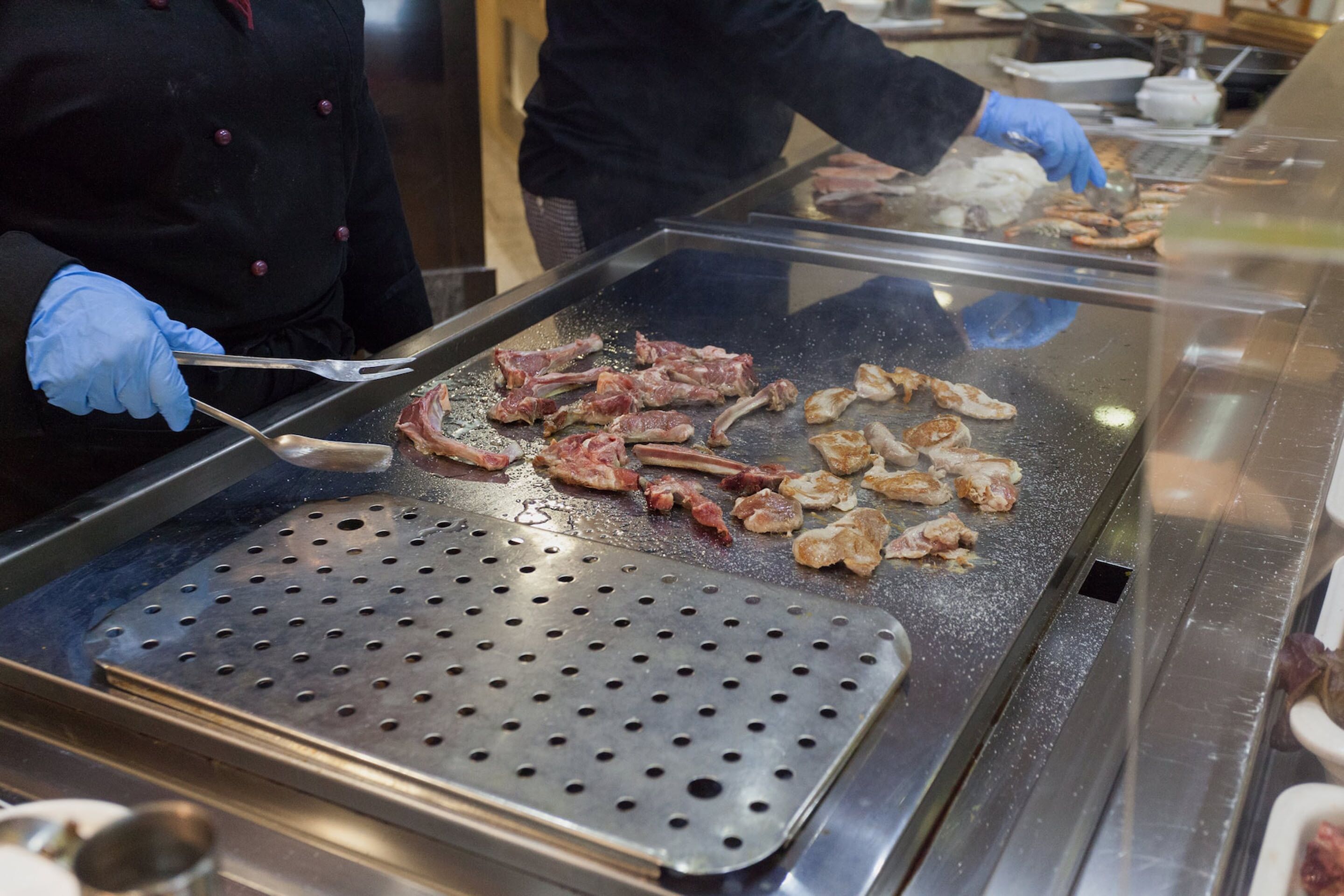 Een keukenhoek met een grill en verschillende vleessoorten die bereid worden.