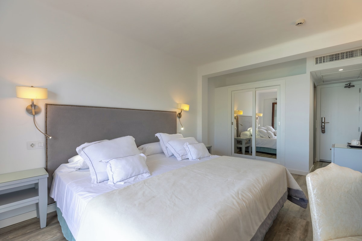 Una habitación de hotel con una cama grande, mesitas de noche, un espejo y un armario.
