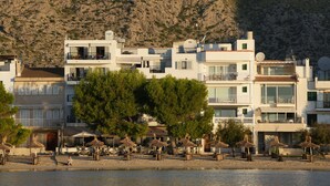 A coastal hotel with multiple floors, outdoor seating, and a rocky hillside backdrop. - Hoposa Bahía (Pollenca)