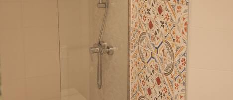 A shower with a glass door and a tiled wall with a geometric pattern.