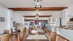 A spacious dining area with wooden tables and chairs, a central serving counter, and a kitchen in the background. - Hoposa Bahía (Pollenca)