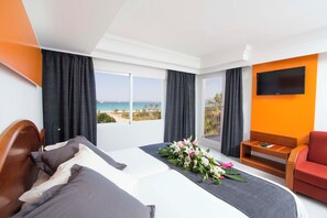 Ein Hotelzimmer mit Bett, Fernseher, Balkon mit Meerblick und einem roten Sessel.
