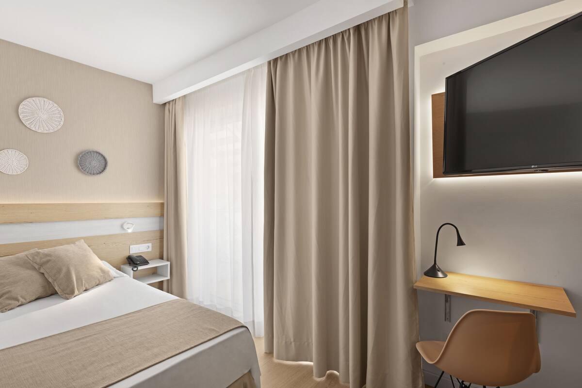 Una habitación de hotel moderna con cama, escritorio, silla, televisor y cortinas.