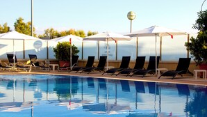 Una piscina con sillones de descanso y sombrillas, rodeada de plantas en macetas.