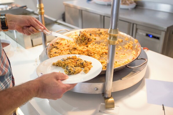 A person serving food from a large, round, metallic pan.