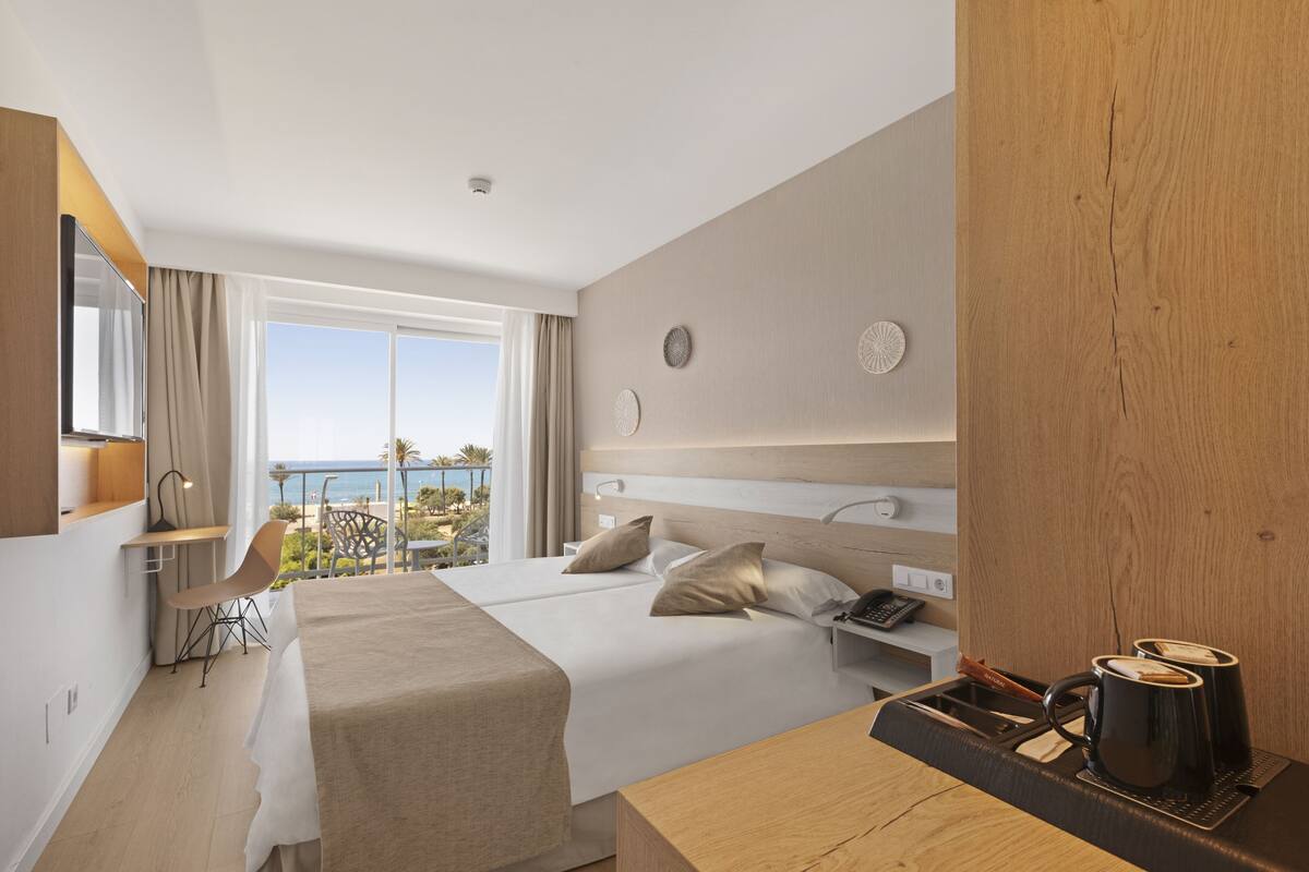 Habitación de hotel con cama, escritorio, silla, cafetera y vista al océano.