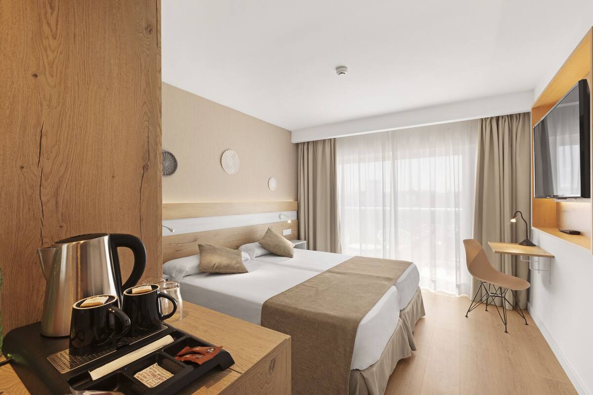 Habitación de hotel con cama, mesita de noche con cafetera y escritorio con silla.