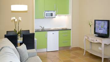 Un espacio habitable compacto con kitchenette, zona de comedor y televisor sobre una mesita.