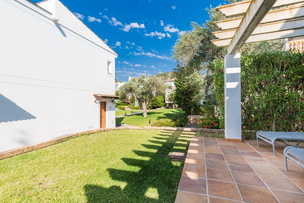 Un patio con un edificio blanco, un patio de baldosas y una pérgola.