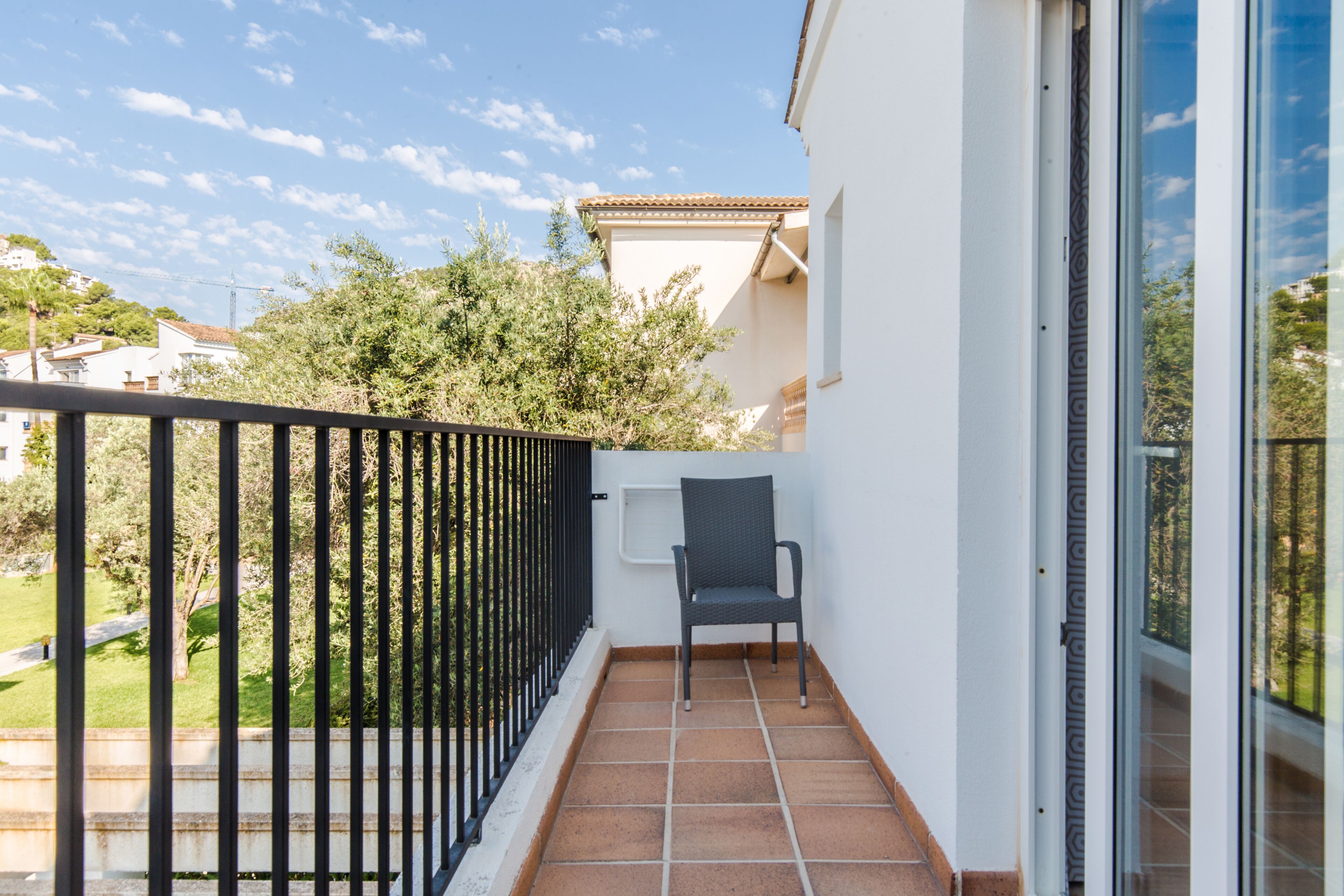 A balcony with a chair, a metal railing, and a view of trees and buildings.