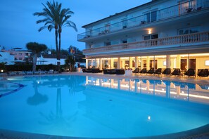 Un hotel con piscina, mobiliario exterior y un edificio de dos plantas con balcones.