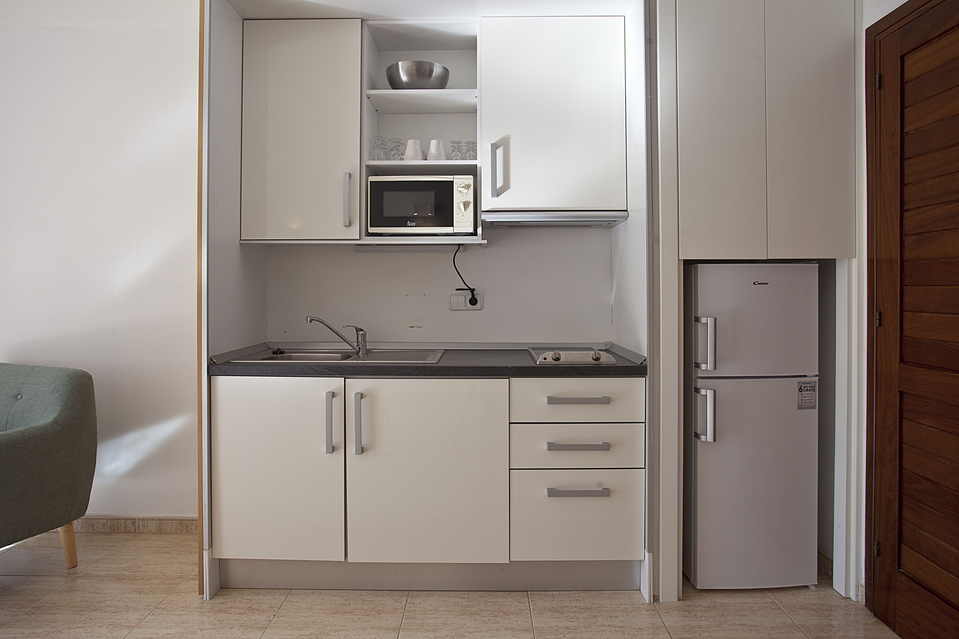 A compact kitchen with white cabinets, a microwave, a sink, and a refrigerator.