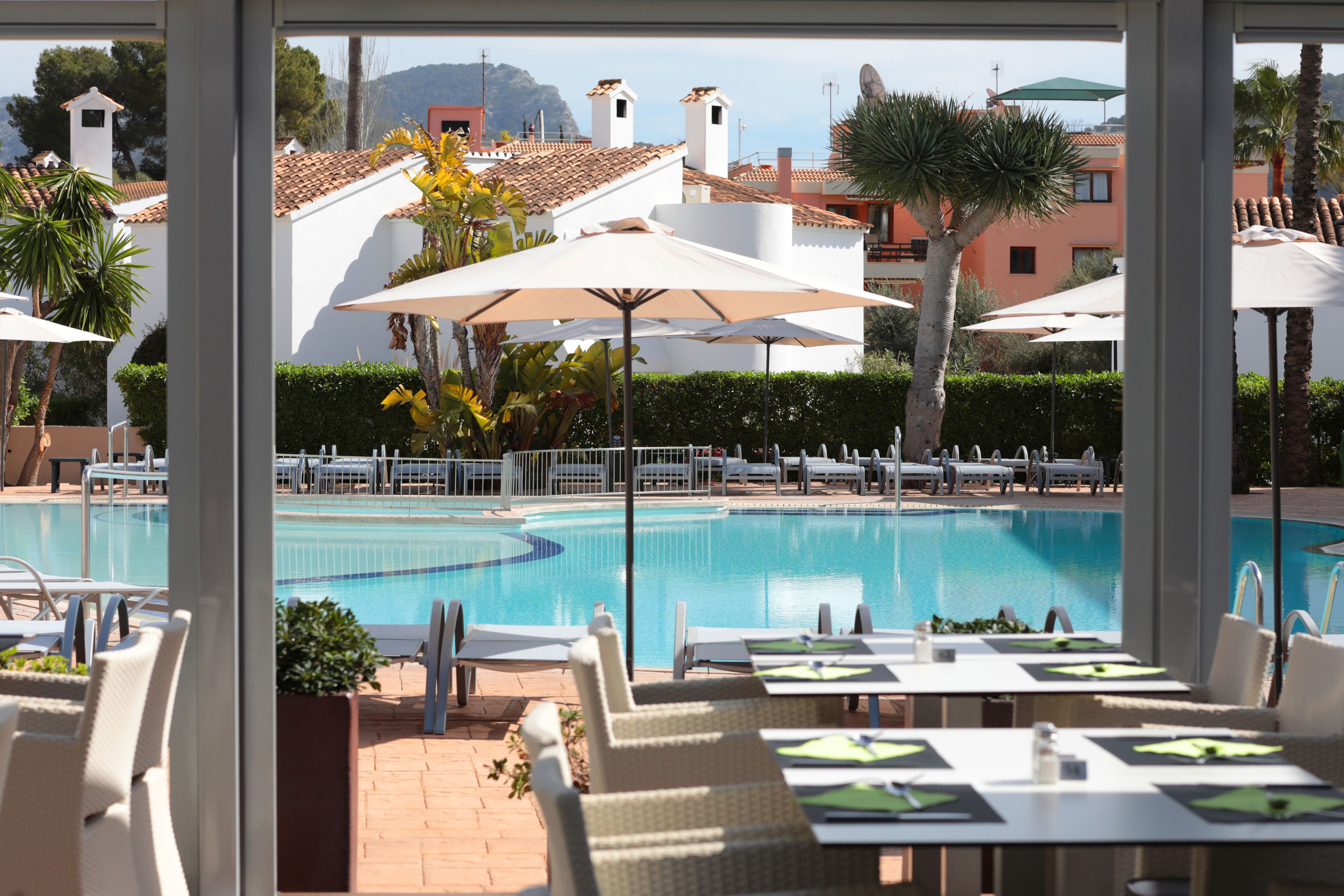 A poolside area with lounge chairs and umbrellas, a pool, and buildings in the background.