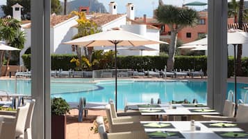A poolside area with lounge chairs and umbrellas, a pool, and buildings in the background.
