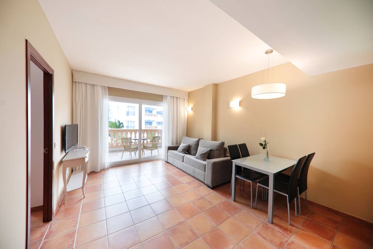 Una sala de estar con sofá, una mesa de comedor con sillas, un televisor sobre un mueble bajo y un balcón con vistas.
