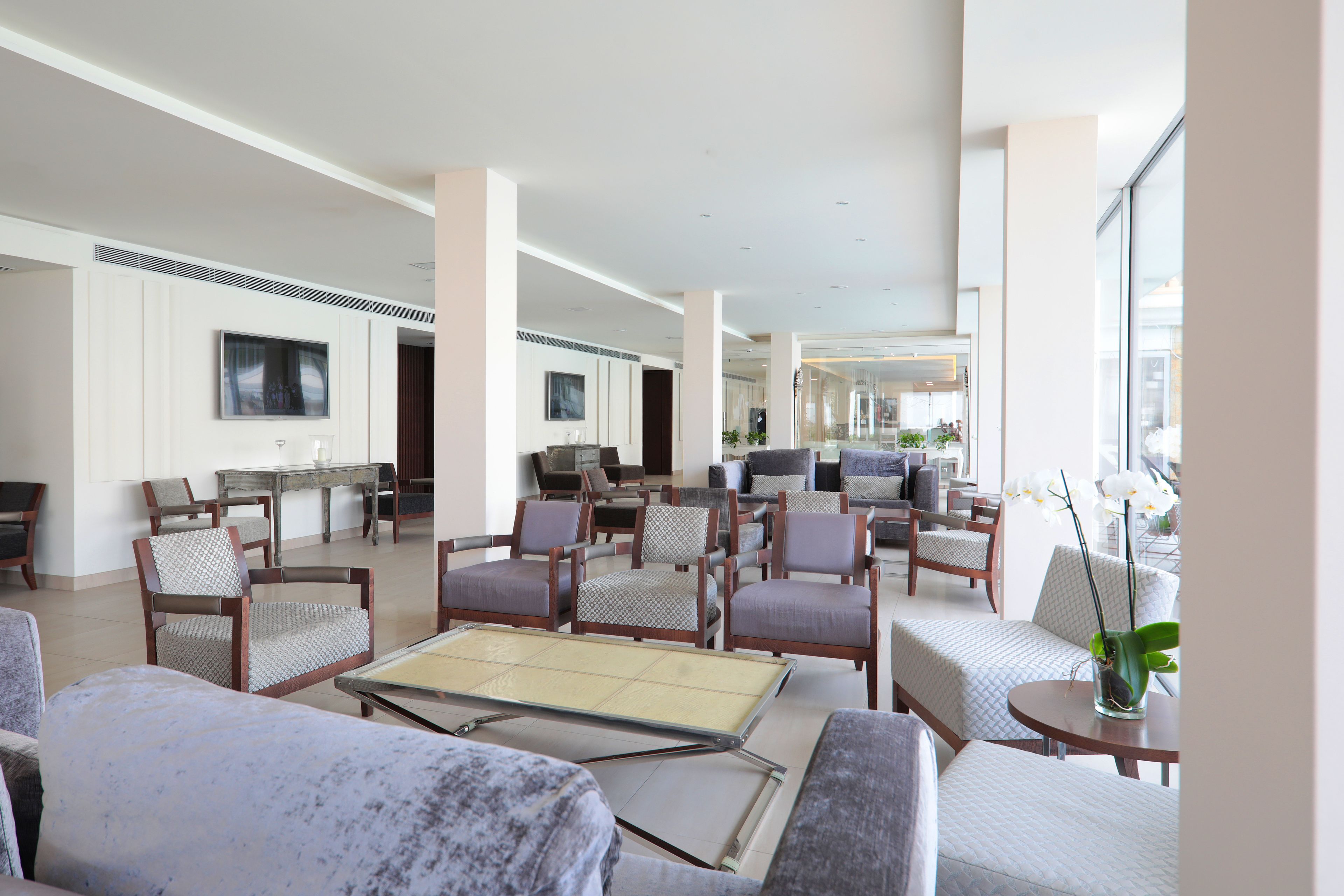 Un vestíbulo amplio con varias zonas de estar, una mesa central y un gran ventanal que proporciona luz natural.