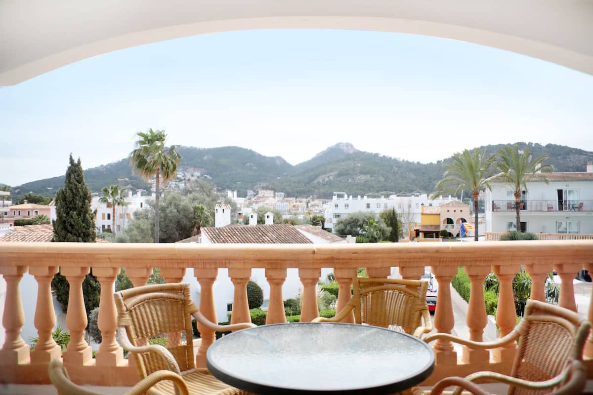 Un balcón con mobiliario de mimbre y vistas a un pueblo con montañas al fondo.
