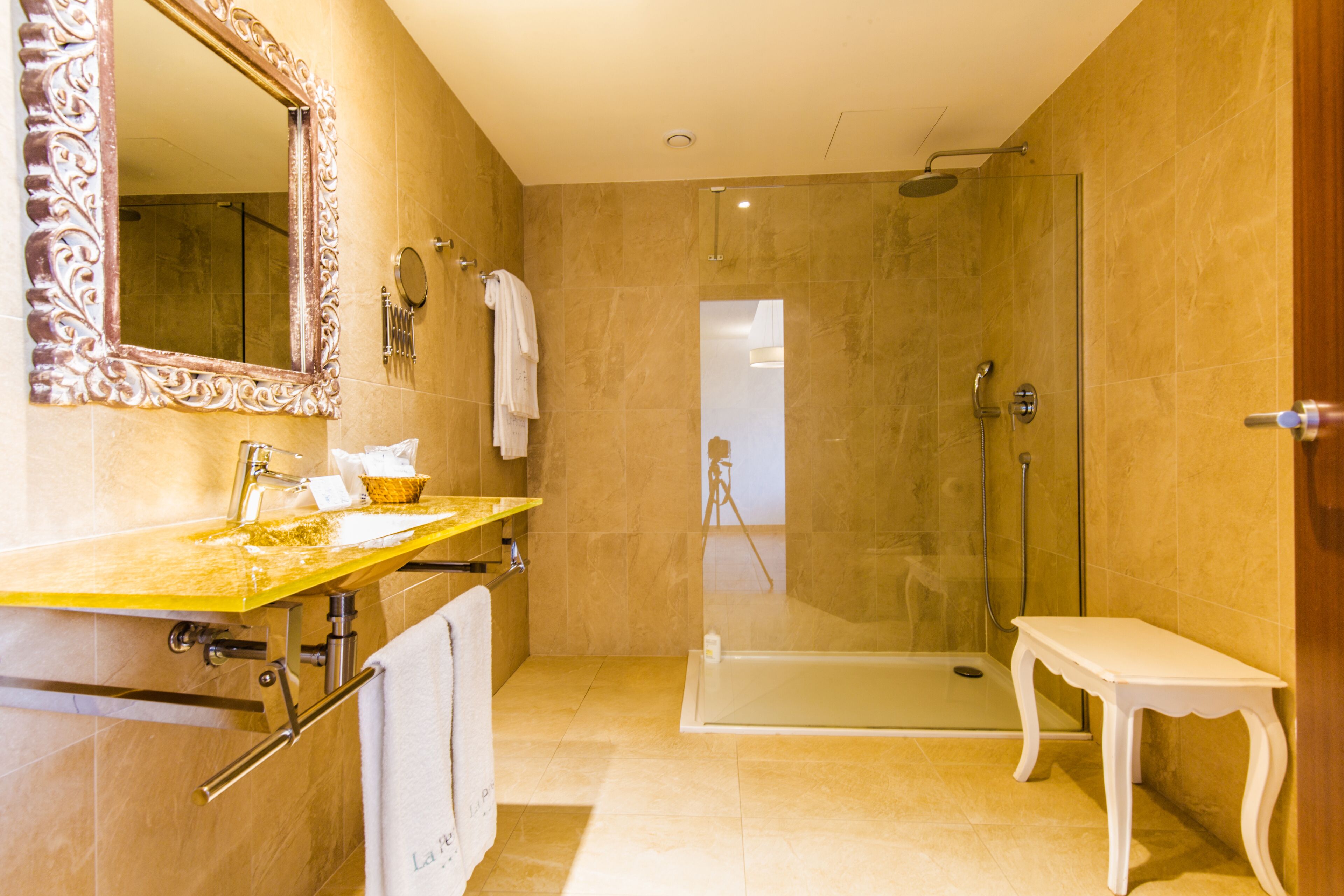 A bathroom with a glass-enclosed shower, a vanity with a mirror, and a small white bench.