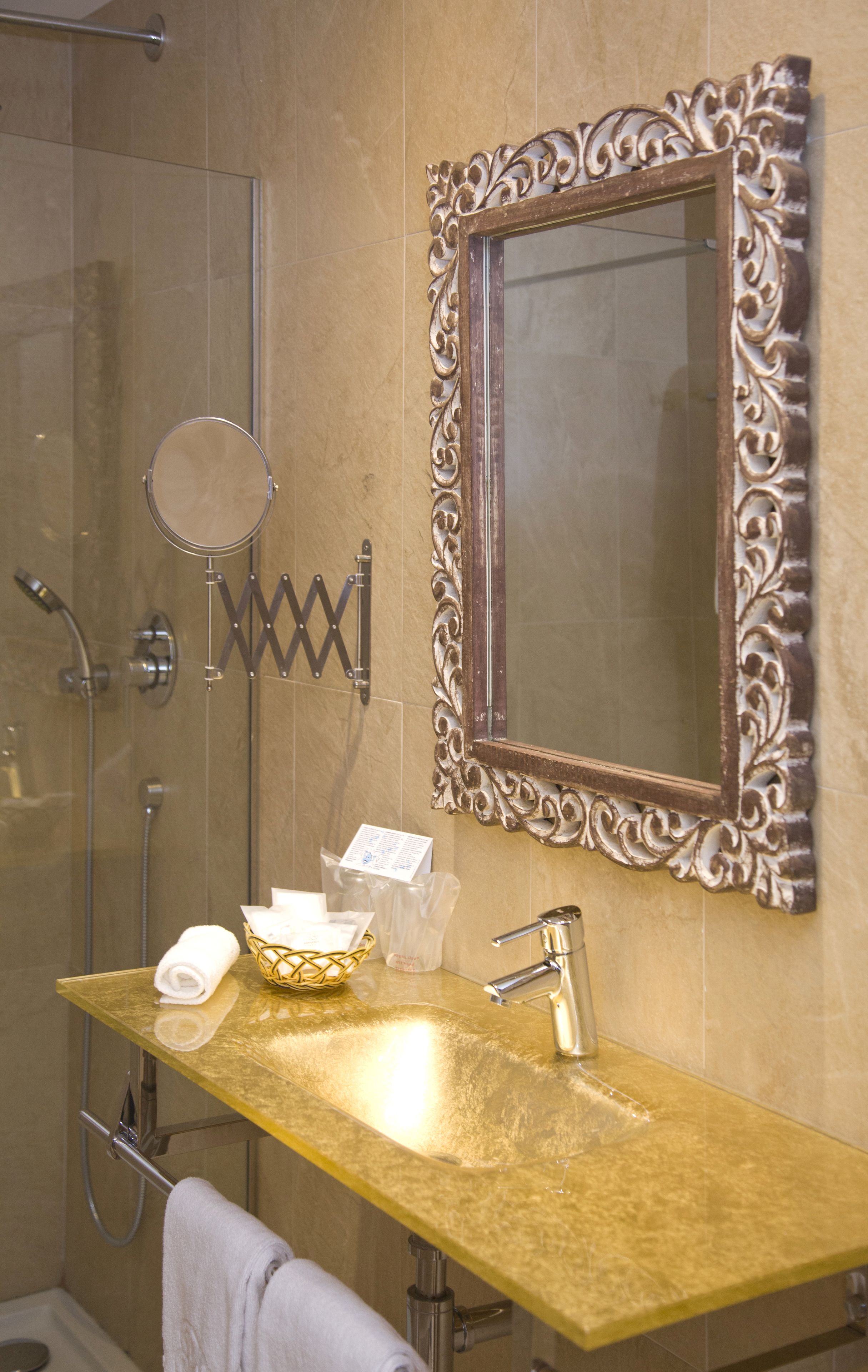 A bathroom with a gold vanity, a large mirror with an ornate frame, a shower, and a towel rack.
