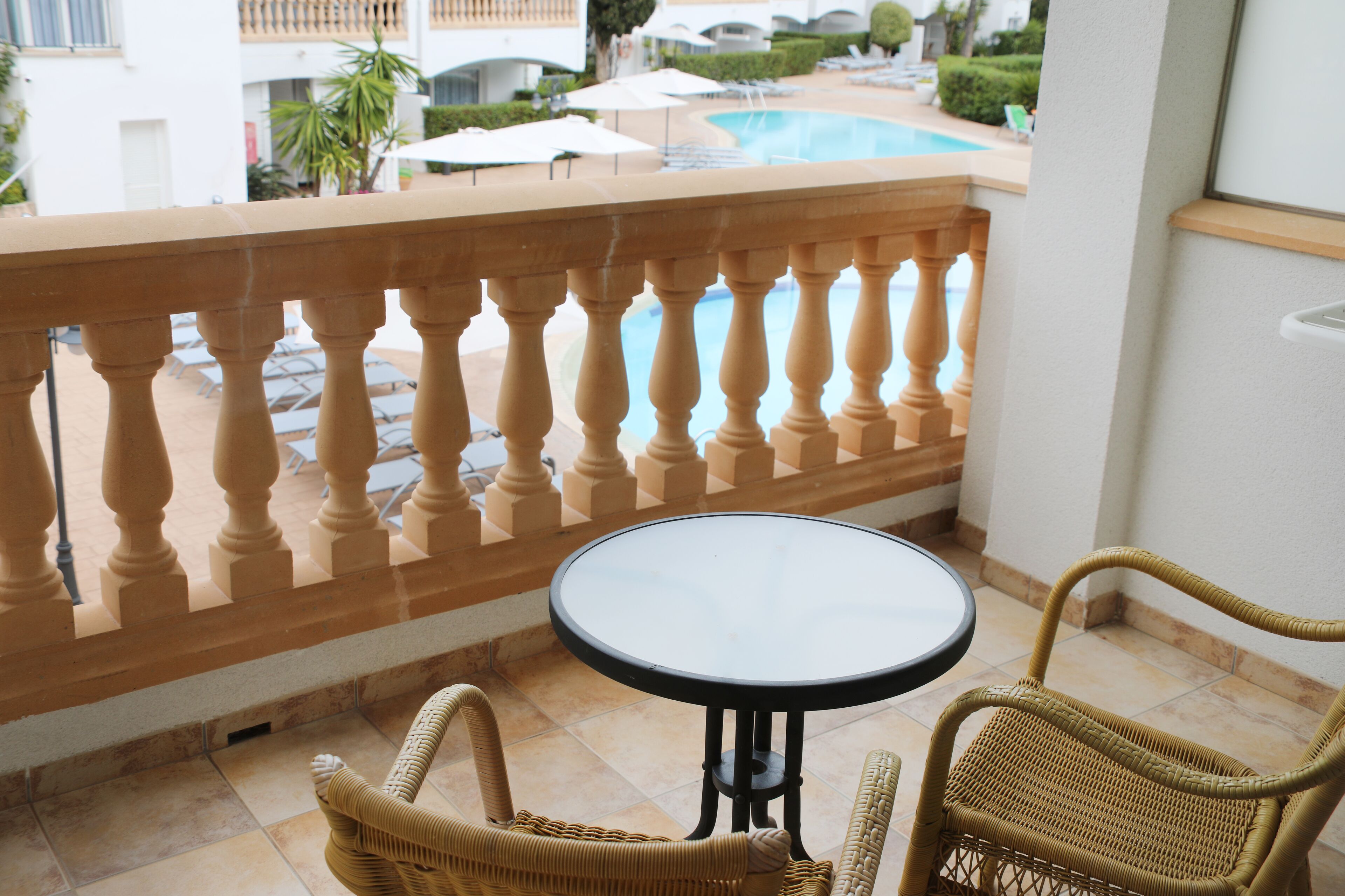 Ein Balkon mit einer Brüstung, einem runden Tisch und Korbstühlen.