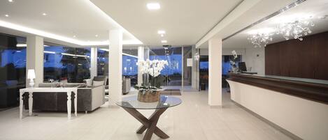 A modern hotel lobby with a glass-top table, a sofa, and a reception desk.
