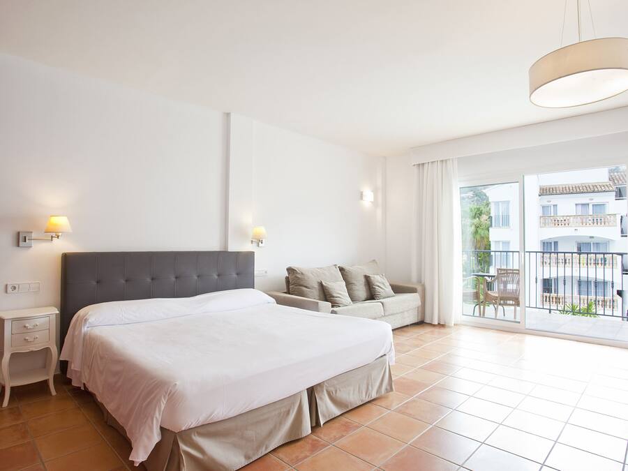 Een slaapkamer met een groot bed, een nachtkastje, een sofa en een balkon met uitzicht op gebouwen.