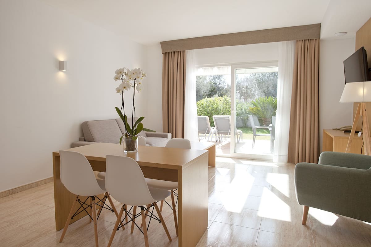 Una habitación de hotel moderna con comedor, sofá, televisor y balcón con mobiliario exterior.