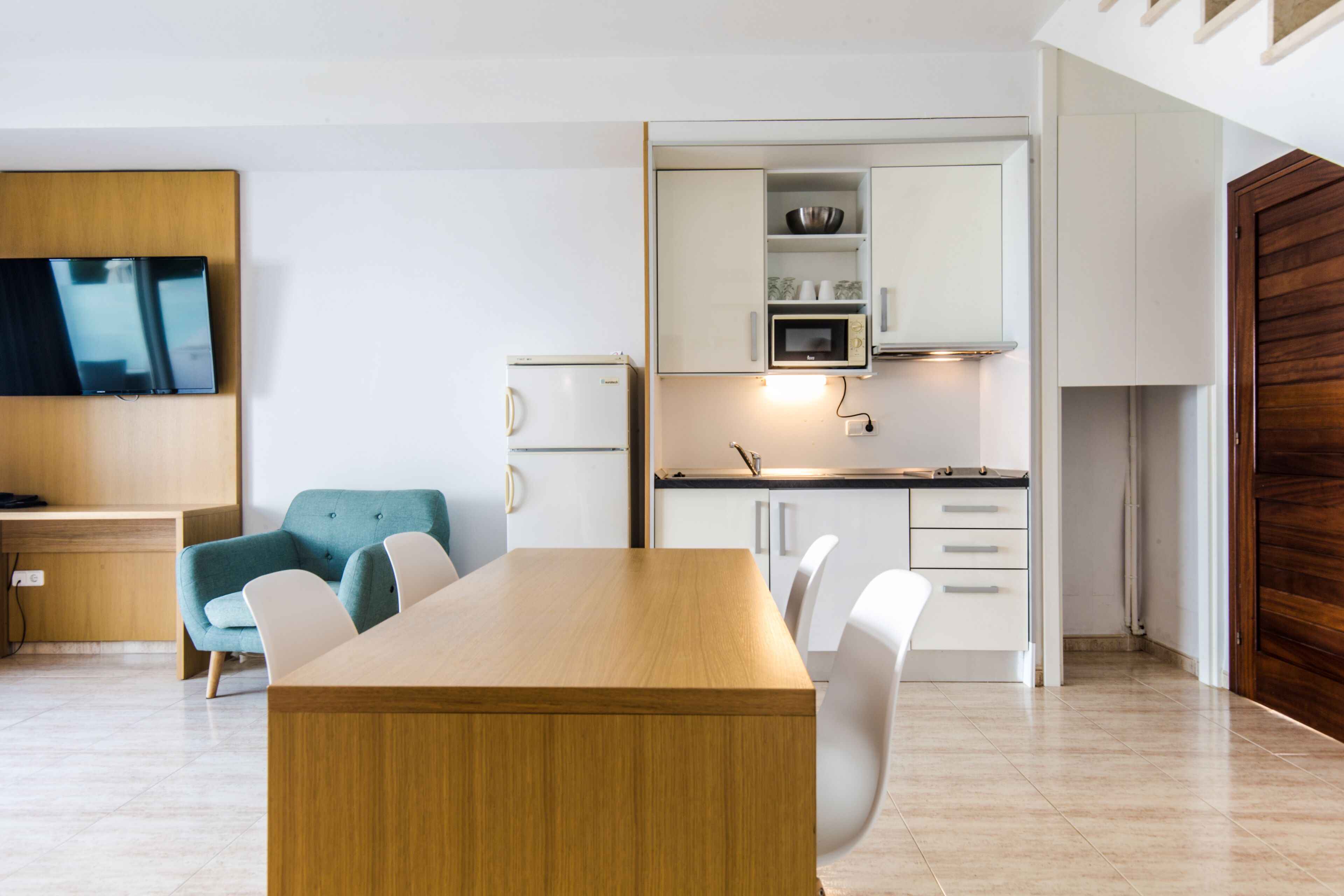 A modern kitchen with white cabinets, a microwave, and a wooden dining table with chairs.