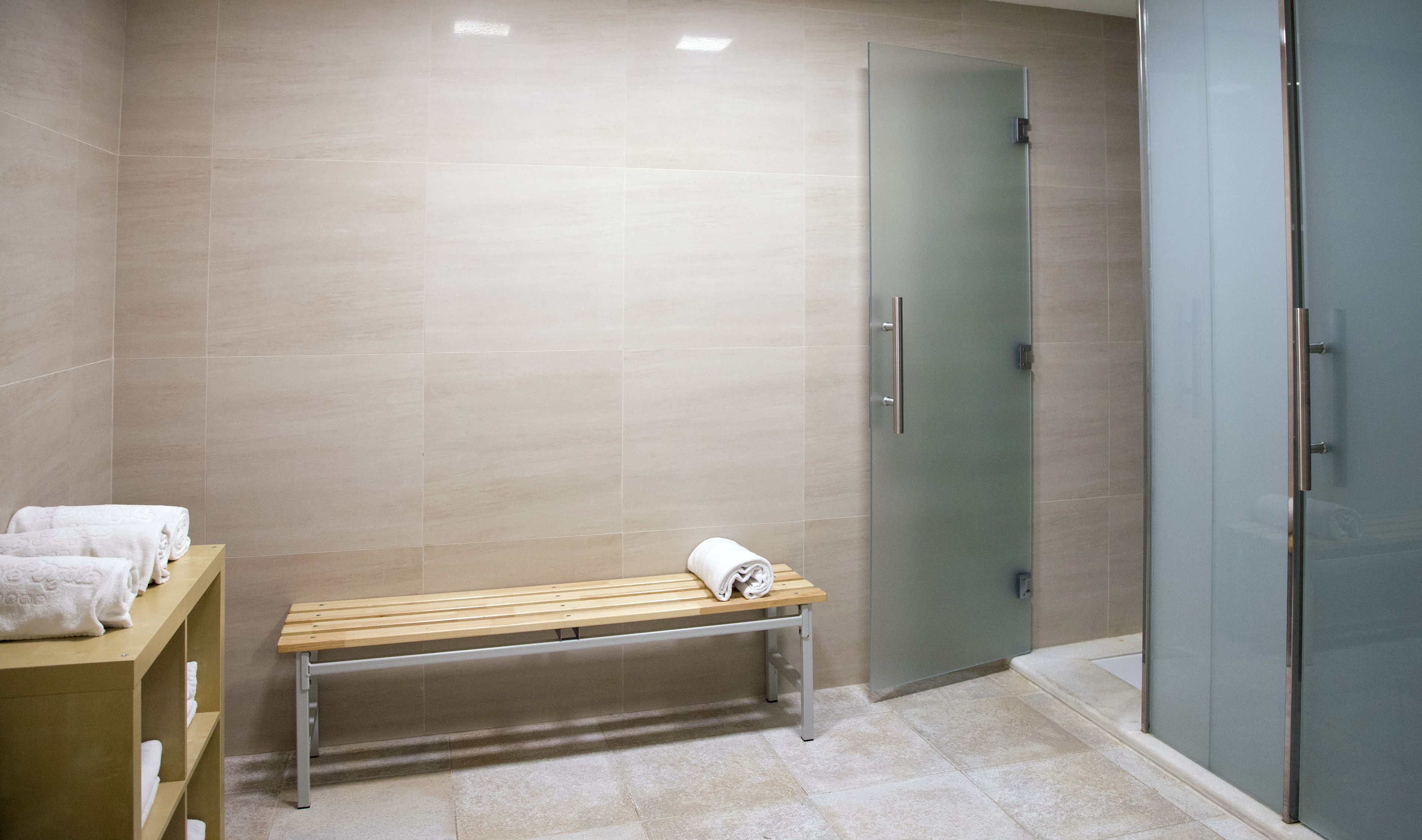 A bathroom with a bench, a glass shower door, and a towel rack.