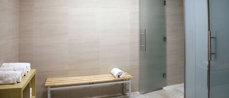 Une salle de bain avec un banc, une porte de douche en verre et un porte-serviettes.