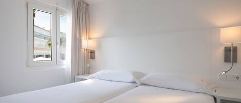 A hotel room with a bed, a nightstand, a lamp, and a window with curtains.