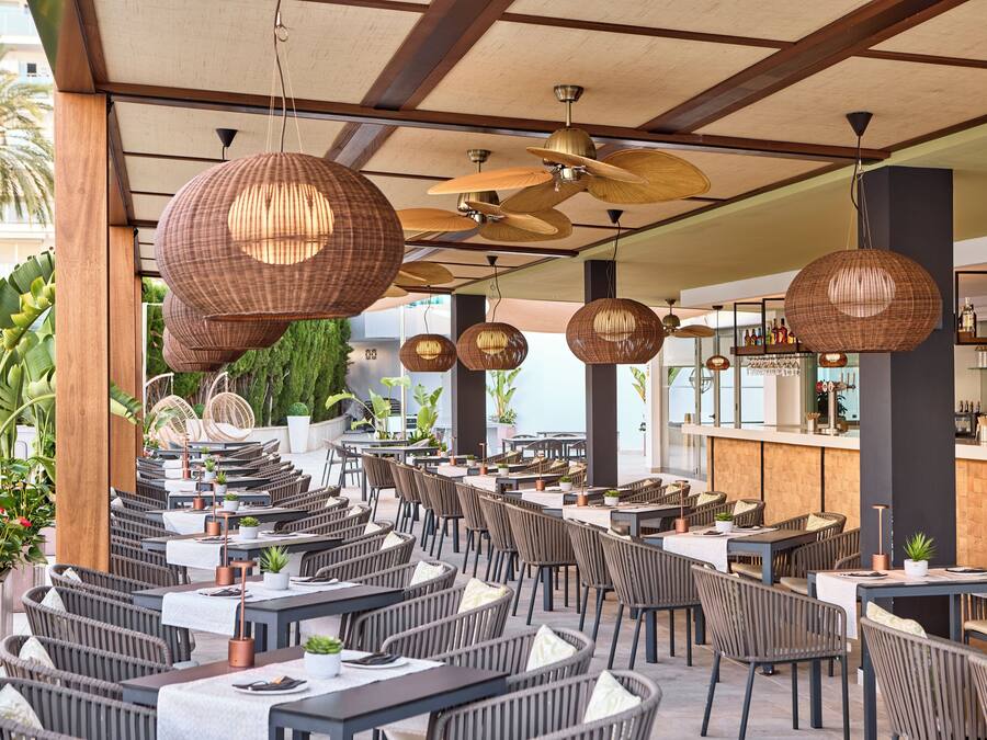 An outdoor dining area with wicker furniture, ceiling fans, and a bar in the background.