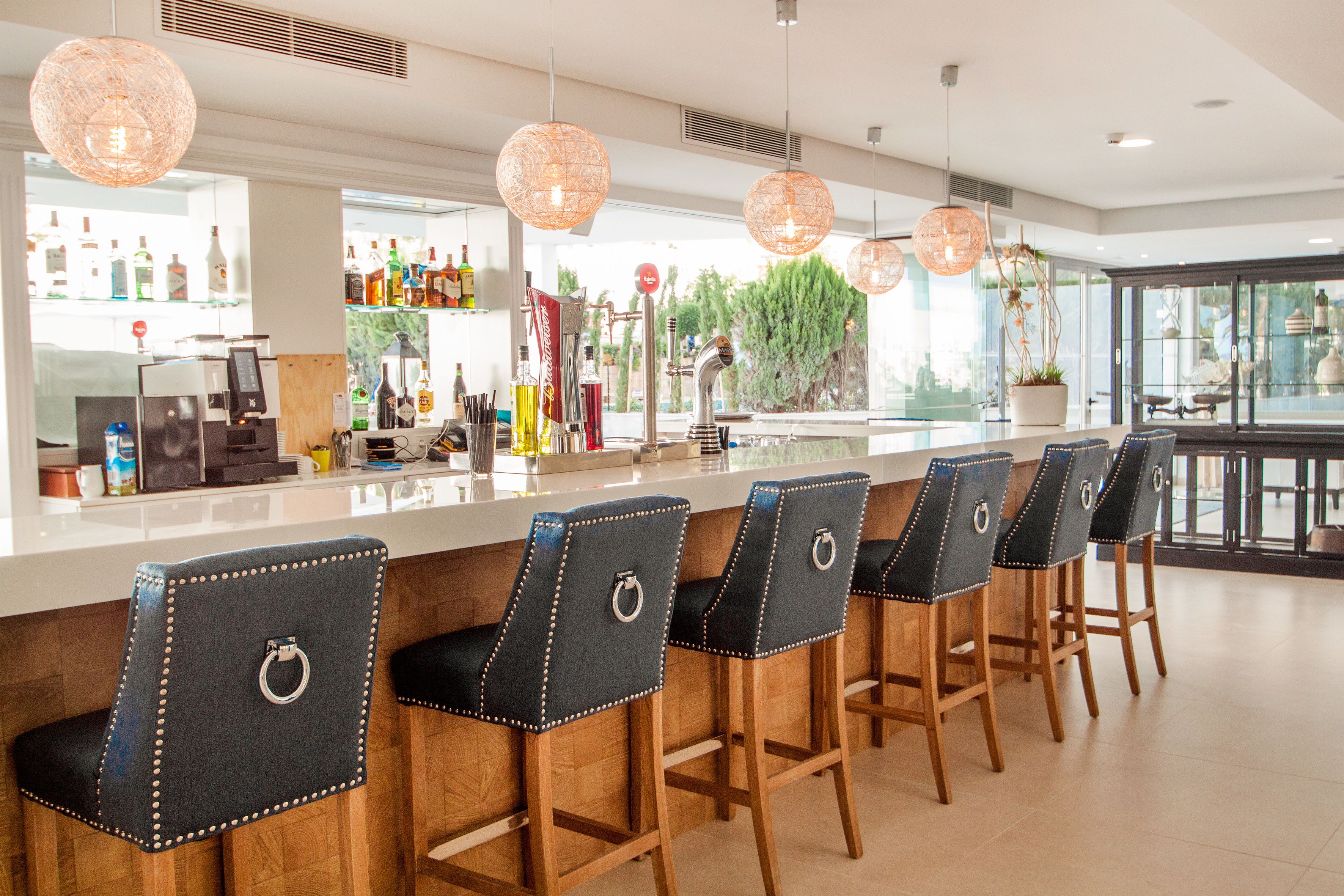 A bar area with wooden bar stools, a bar counter, and pendant lighting.