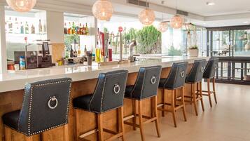 A bar area with wooden bar stools, a bar counter, and pendant lighting.