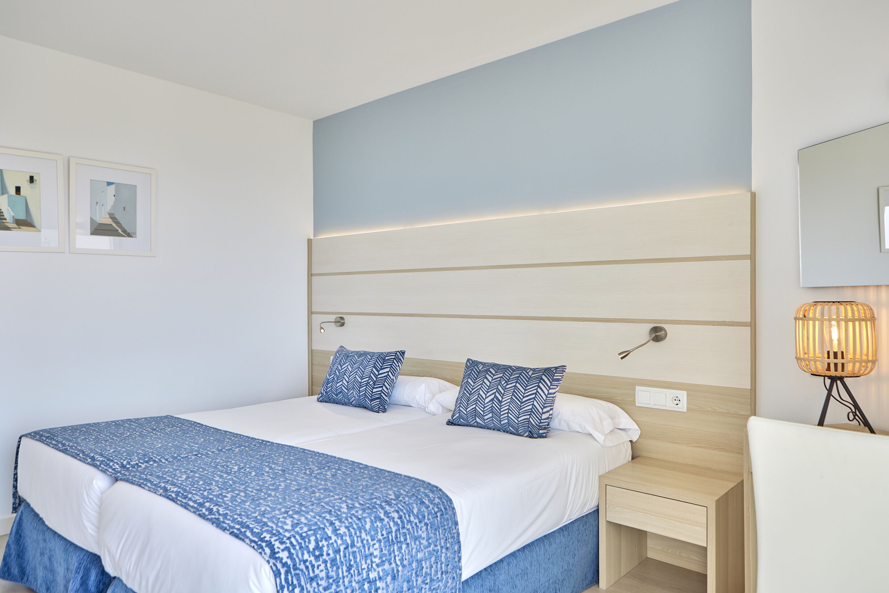 A modern hotel room with a large bed, bedside tables, a bedside lamp, and framed artwork on the wall.