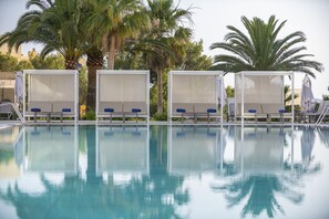 Un área de piscina con sillones de descanso y palmeras.