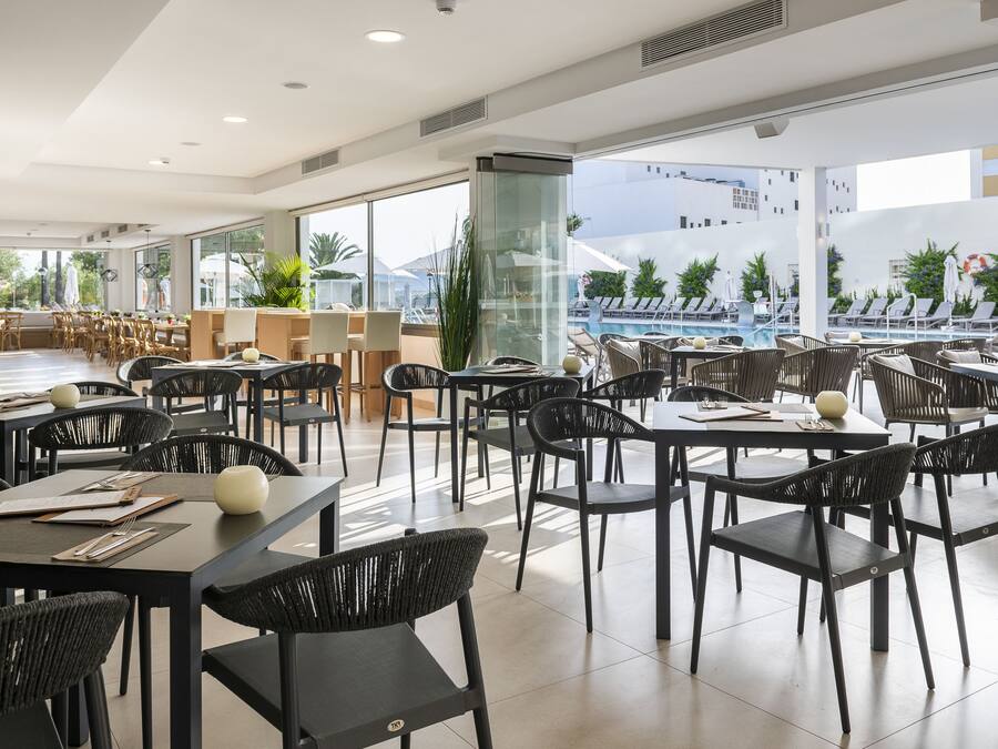 Un restaurante moderno con sillas y mesas de mimbre negro, ventanas amplias y vista a una piscina.