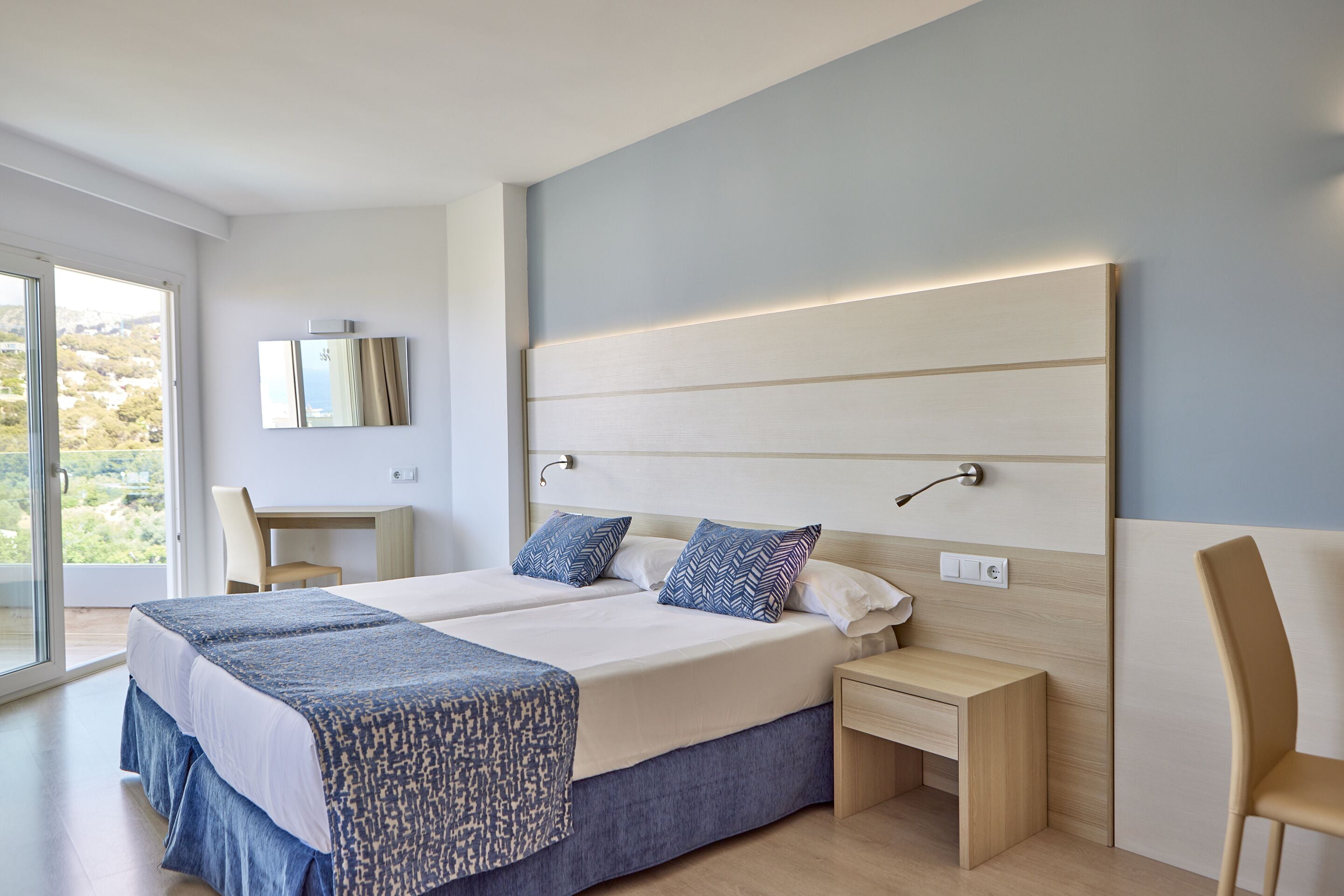 A modern hotel room with a large bed, bedside tables, a desk, and a chair.