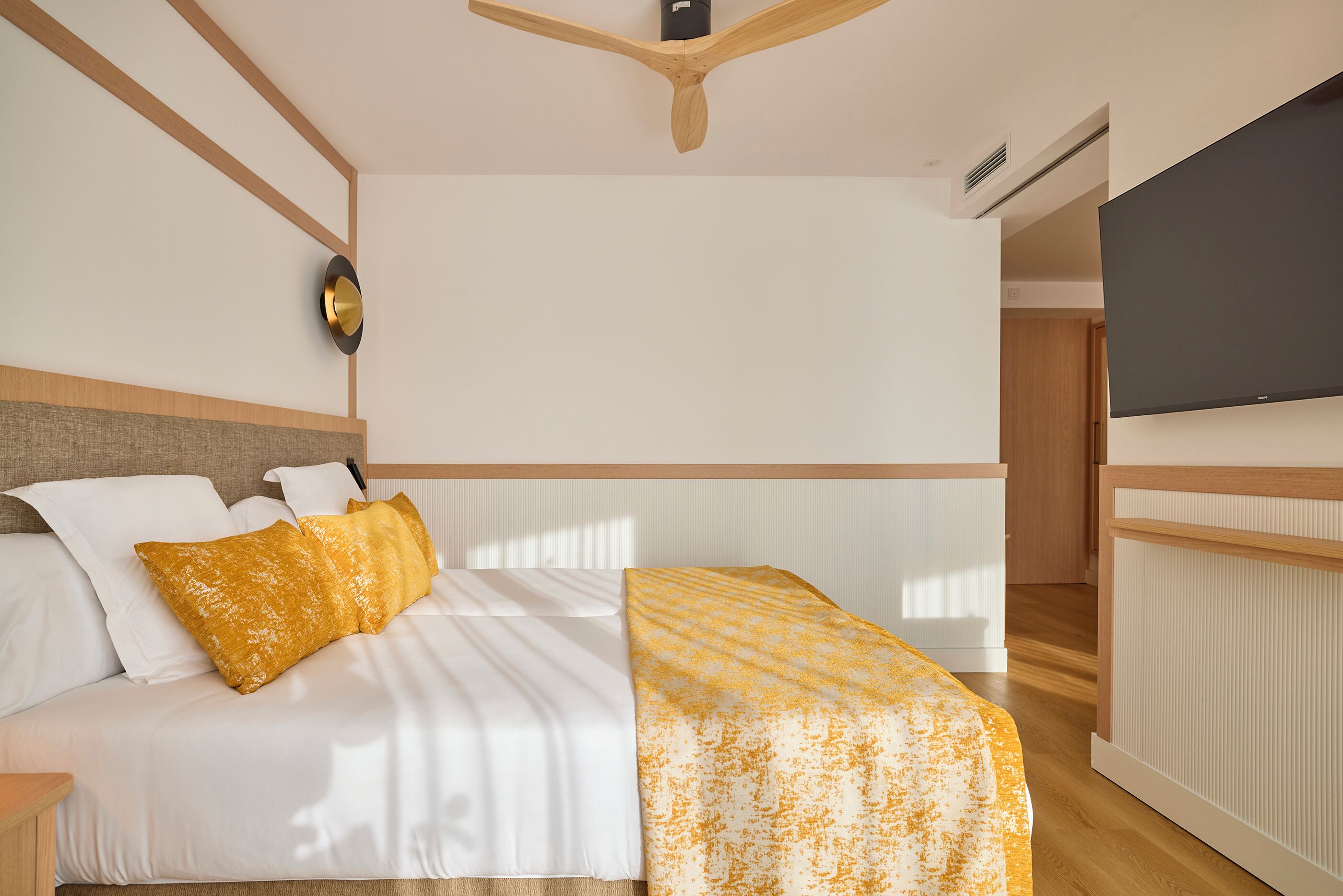 Una habitación de hotel moderna con cama, mesita de noche, televisión y un diseño de techo de madera.