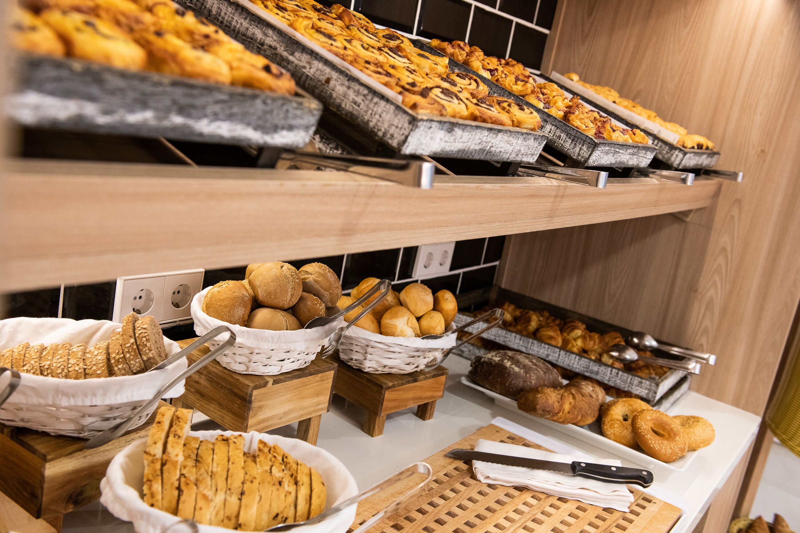 Variedad de productos horneados expuestos en estantes y cestas, incluyendo pan, pasteles y rosquillas.
