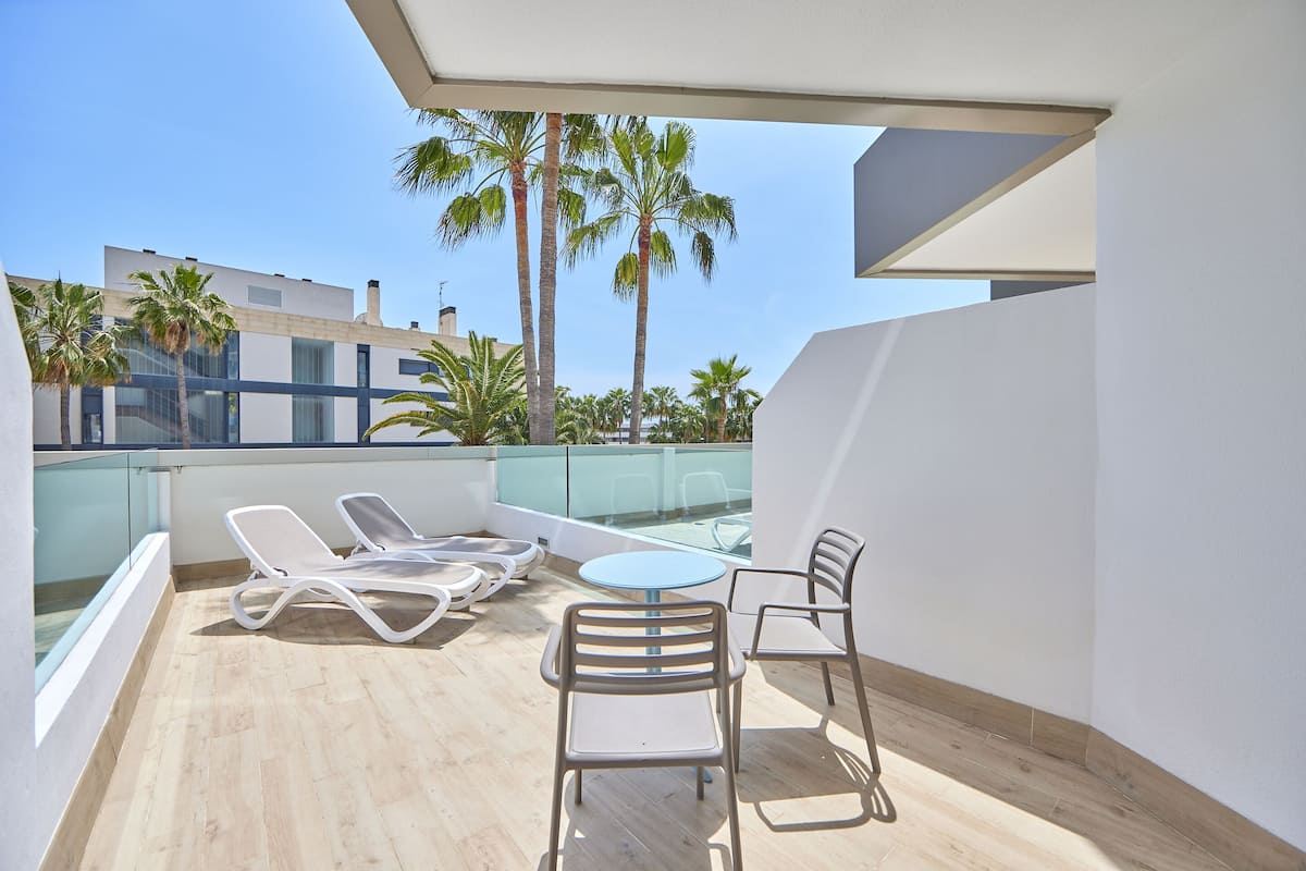 A balcony with a table and chairs, overlooking palm trees and buildings.