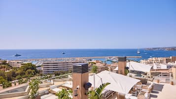 Une terrasse sur le toit avec des sièges extérieurs, une vue sur la mer et une marina en arrière-plan.