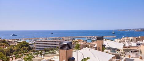 Terraza en la azotea con mobiliario exterior, vista al mar y un puerto deportivo al fondo.