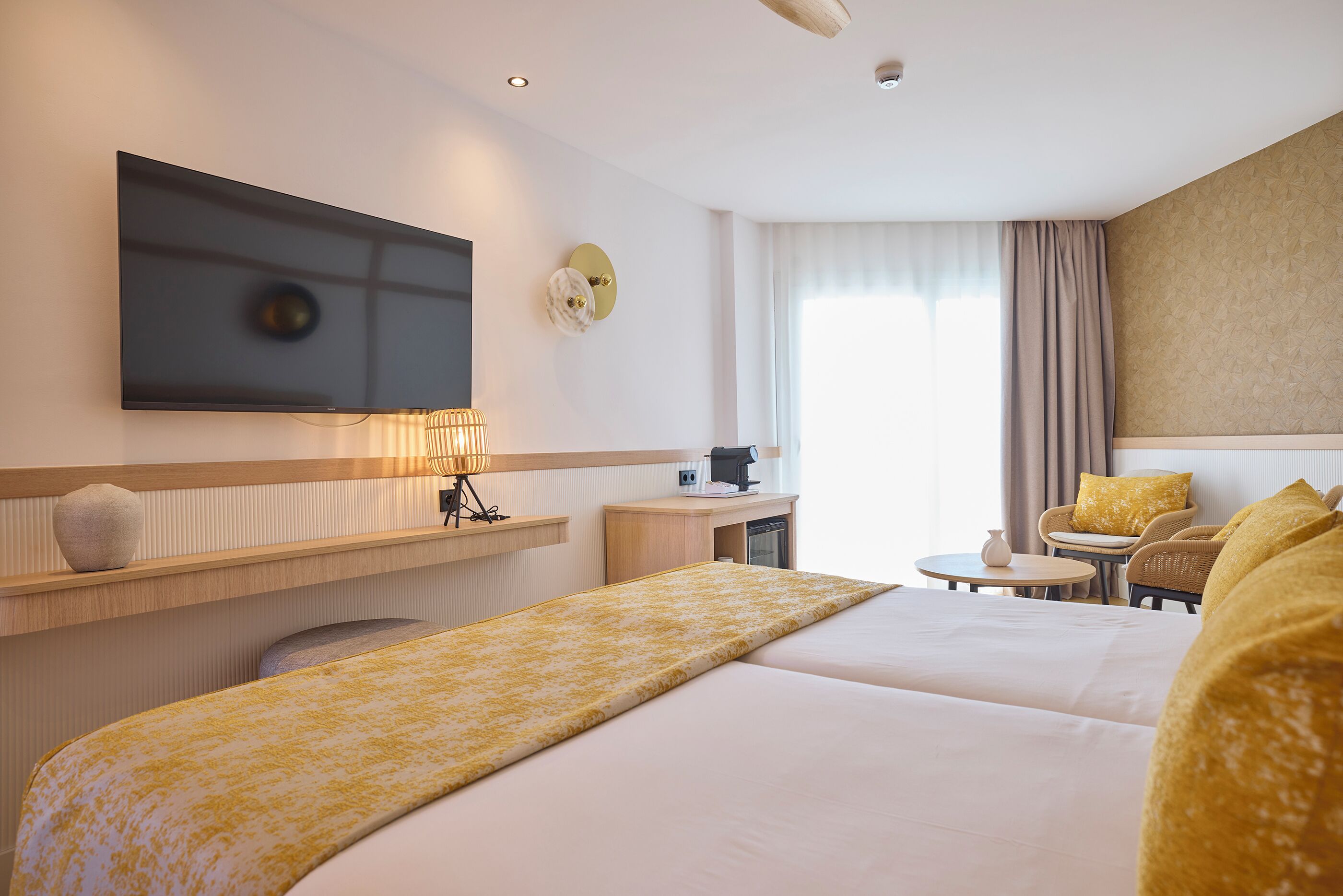 Habitación de hotel con una cama grande, un escritorio con lámpara, televisor y una zona de estar con sillas y una mesita.