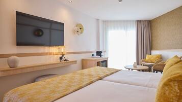 Habitación de hotel con una cama grande, un escritorio con lámpara, televisor y una zona de estar con sillas y una mesita.