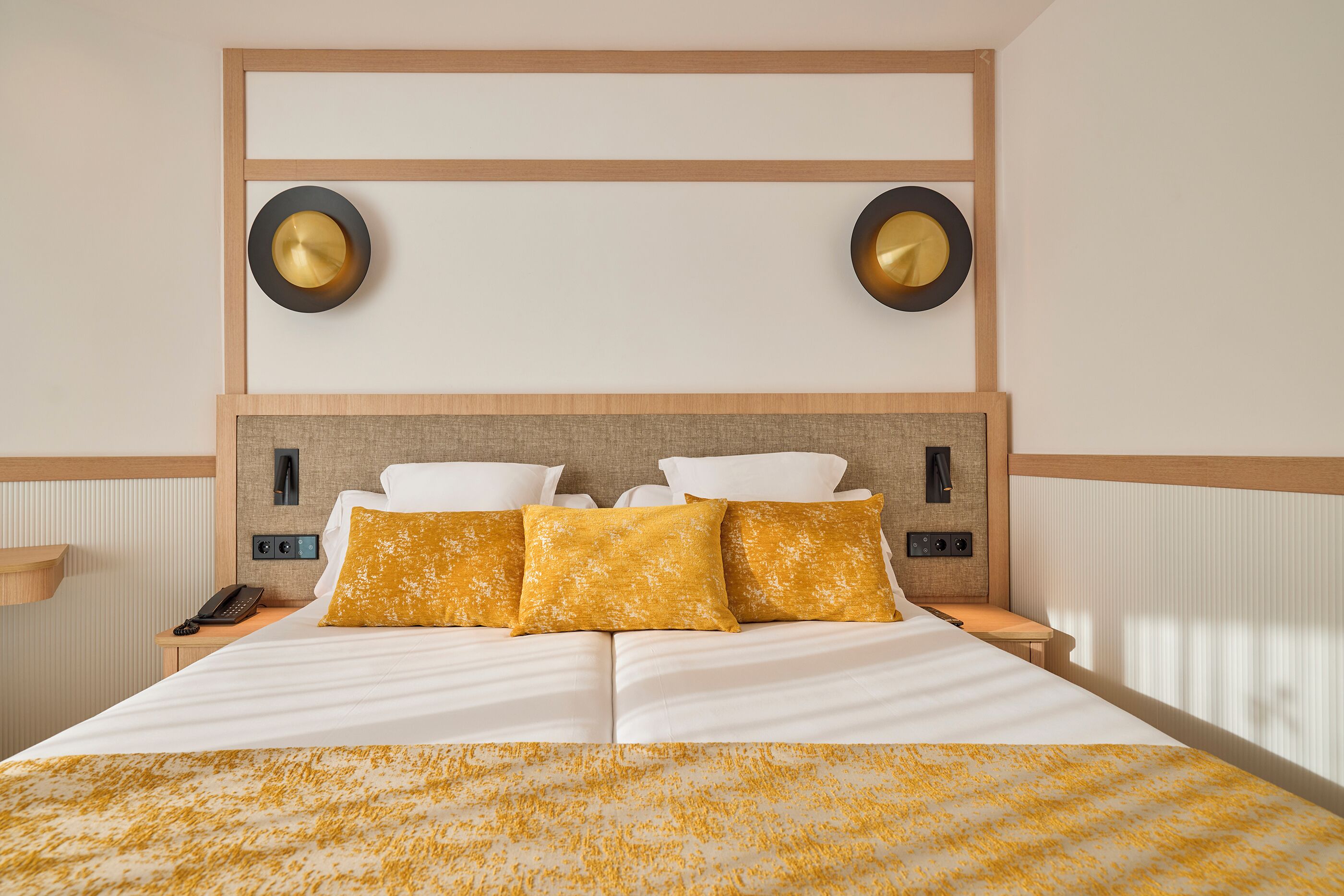 A hotel room with a large bed, two bedside tables, a wall-mounted phone, and two wall sconces.