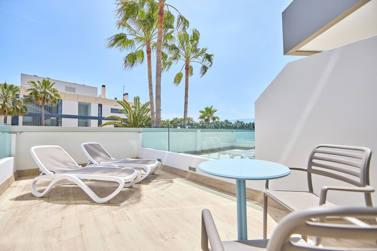 A rooftop terrace with lounge chairs, a table, and a view of palm trees and buildings.