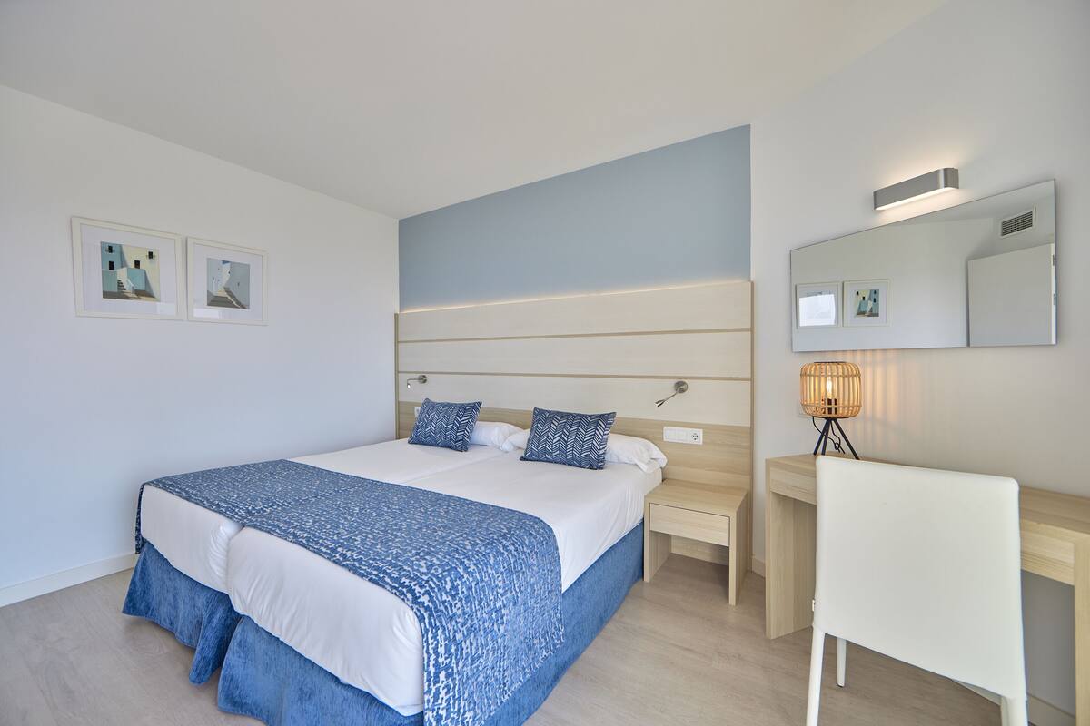 A bedroom with a bed, bedside tables, a desk, a chair, and a lamp.